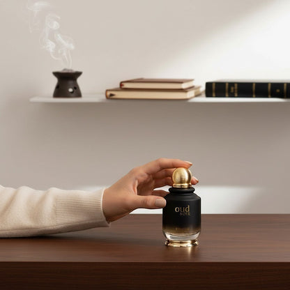 Oud Sera Khadlaj Oud Noir perfume bottle with gold cap held by a hand on a wooden table with incense in the background